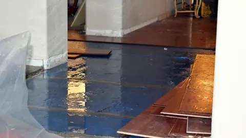 Wood flooring planks lifted from a wet subfloor beside plastic sheeting